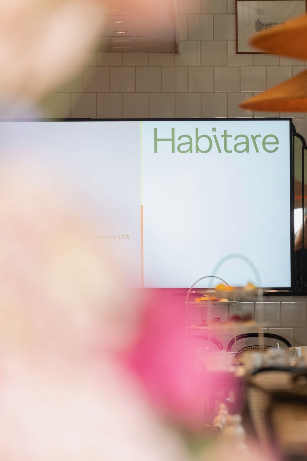 Habitaren logo näytöllä kukkien takaa Afternoon Tea -vaikuttajatapahtumassa